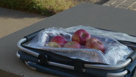 Slider-move-in-of-a-basket-of-fresh-apples-sitting-on-a-picnic-table-in-a-public-park