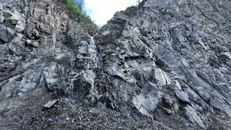 A-stunning-waterfall-flows-gracefully-over-steep-rocky-cliffs,-surrounded-by-the-serene-beauty-of-Yakutia's-natural-landscape-under-bright-morning-skies