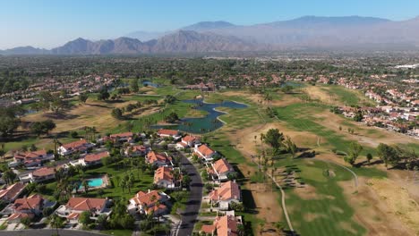 Drone-Retrocediendo-En-ángulo-Alto-Sobre-Casas-En-Palm-Springs,-California,-EE.-UU.,-Con-Campo-De-Golf-Y-Montañas-A-La-Vista