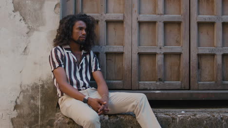 Cool-and-mysteriously-looking-Arabic-black-man-sits-under-a-giant-wooden-door-of-an-old-house