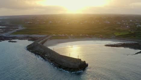 Aerial-dolly-shot-descending-to-Spiddal's-East-Pier,-beautifully-backlit-by-a-stunning-sunset