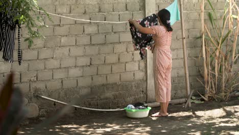 Mujer-Asiática-Colgando-Ropa-Para-Secarla-En-Su-Patio-Trasero-En-Una-Isla-Tropical-En-Lombok,-Indonesia