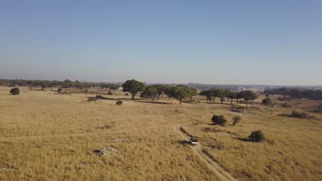 Toma-Aérea-De-Turistas-Que-Viajan-En-Un-Vehículo-Todoterreno-De-Safari-A-Través-De-La-Selva-Africana-Durante-La-Estación-Seca