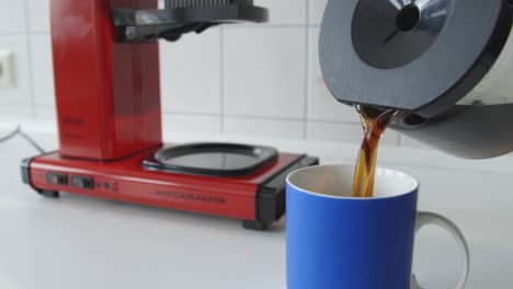 Caucasian-male-hands-pouring-coffee-from-a-vintage-coffee-maker-into-blue-cup