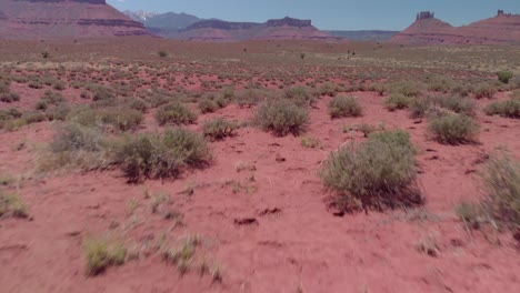 Low-aerial-tilt:-Flight-along-red-scrub-desert-toward-mesas-and-towers