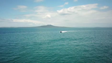 Aerial-drone-shot,-of-a-fast-boat-travelling-towards-the-camera-with-Rangitoto-Island-as-background-in-New-Zealand