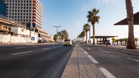 Low-angle-rising-timelapse-of-a-busy-street-along-side-a-boardwalk-in-Tel-Aviv,-Israel-with-cars,-cyclists,-and-pedestrians-on-a-summer-day