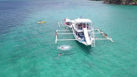 Aerial-view-of-Tourist-doing-backflip-off-a-Tour-boat-into-blue-ocean