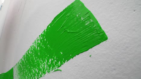 Close-up-slow-motion-of-a-hand-painting-a-white-wall-bright-green-with-a-paint-brush