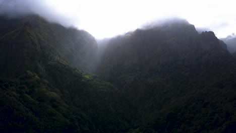 The-beautiful-lush,-green-mountains-of-Madeira,-Portugal-with-the-sunlight-peeking-through-the-misty-mountaintops---Aerial-shot