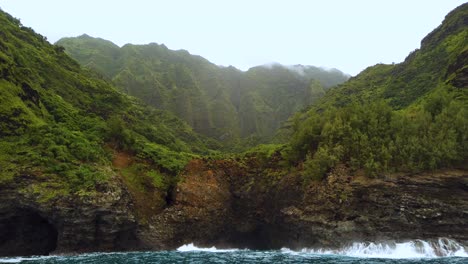 4k-Hawaii-Kauai-Bootfahren-Auf-Meereswellen,-Die-An-Felsiger-Küste-Brechen,-Mit-Bergen-In-Wolkiger-Ferne