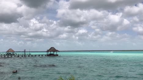 Ein-Boot-Segelt-In-Der-Ferne-über-Die-Lagune-Von-Bacalar,-Während-Das-Wasser-Im-Sonnenlicht-Seine-Farbe-ändert