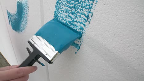 Close-up-slow-motion-of-a-hand-painting-a-blue-letter-on-a-white-wall-with-a-paint-brush