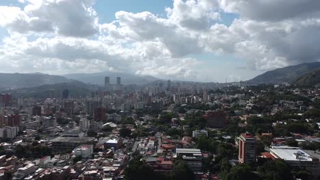 Aerial-of-downtown-Caracas-Venezuela,-rolling-hills,-billowing-clouds,-full-sun,-dolly-back