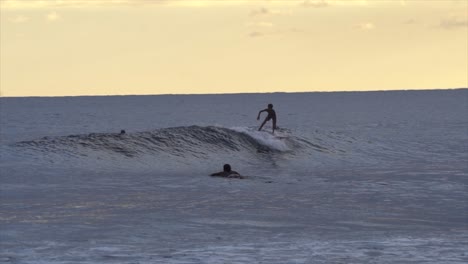 Joven-Surfista-En-Cámara-Lenta-Cogiendo-Olas-En-Una-Puesta-De-Sol-De-Color-Naranja-Quemado,-Indonesia