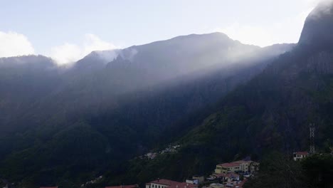 Ein-Blick-Auf-Die-Verträumte-Landschaft-Der-Berge-Von-Madeira,-Portugal-Mit-Gebäuden-Und-Häusern-Am-Berghang-Und-Dem-Sonnenlicht,-Das-über-Die-Berggipfel-Lugt---Weitwinkelaufnahme