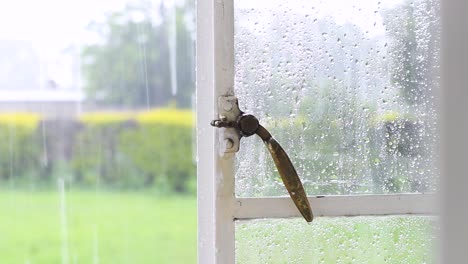 Close-up-shot-of-a-hand-closing-a-window-in-a-green-meadow-background-on-a-cloudy-rainy-day,-looking-out-of-a-window-at-home-by-end-of-day-while-it's-raining-Harare,-Zimbabwe