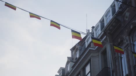 Panning-rotational-shot-of-small-Belgian-flags-hanging-up-and-waving-slightly-in-the-street-of-the-city-center-on-a-cloudy-day-in-Brussels,-Belgium