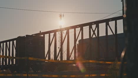 Freight-Train-Cargo-Coming-to-a-Stop-During-Golden-Hour-with-Sun-Flares-Shining-Through-Empty-Train-Carts-Cinematic