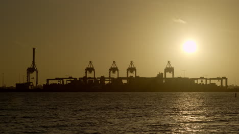 Silhouette-of-shipping-yard-at-sunset,-sun-low-in-sky