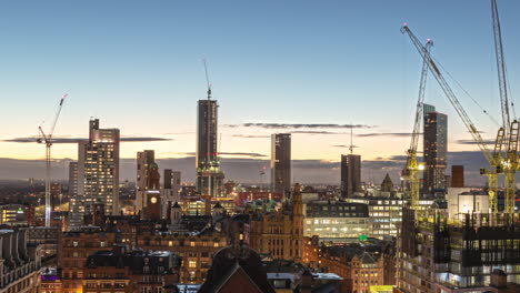 Sunset-time-lapse-view-of-the-Manchester,-UK-skyline-with-several-construction-cranes-moving-and-working-to-construct-new-buildings