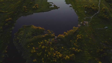 Aerial-view-over-a-pond-and-a-forest-road,-during-sunset,-on-the-countryside-of-Ukraine---tilt-up,-drone-shot