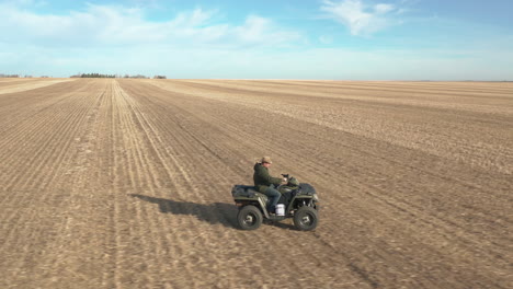 Man-driving-with-atv-in-vast-farm-fields,-aerial-lateral-follow