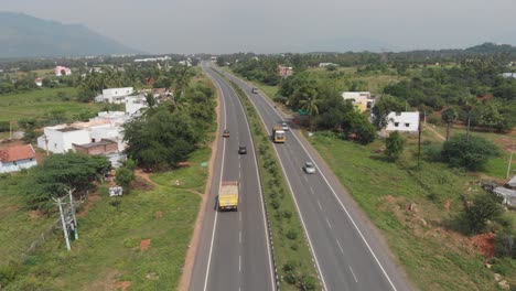 Volando-Sobre-Una-Carretera-En-La-India-Rodeada-De-Exuberantes-Campos-Verdes-En-El-Fondo-Cubiertos-De-Vegetación.