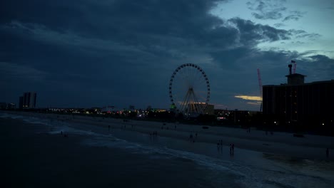 Illuminated-amusement-park-at-night-on-the-ocean-front-with-waving-ocean