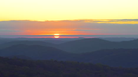 Sunrise-over-two-large-hills-with-glassy-mountain-in-the-distance