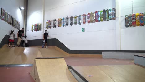 Wide-shot-of-male-skateboarder-jumping-high-over-ramp-inside-indoor-skateboard-park