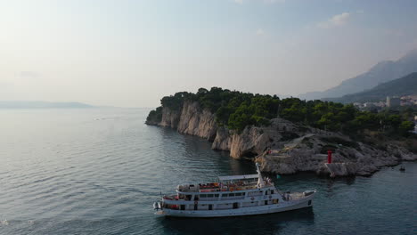 Barco-De-Ferry-Local-Llegando-Al-Puerto-De-La-Ciudad-De-Makarska-Al-Atardecer,-Vista-Aérea