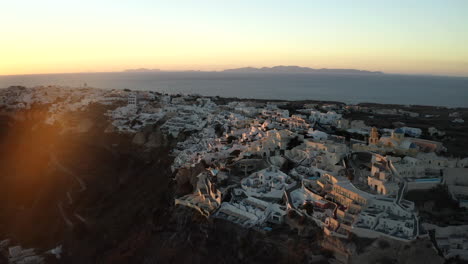 Oia-Santorini-island-sunset-drone-shot-overlooking-white-buildings-and-the-sea,-Greece-in-4K