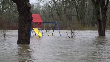 Flood-water-engulfs-colorful-playground-equipment,-creek-jumps-bank