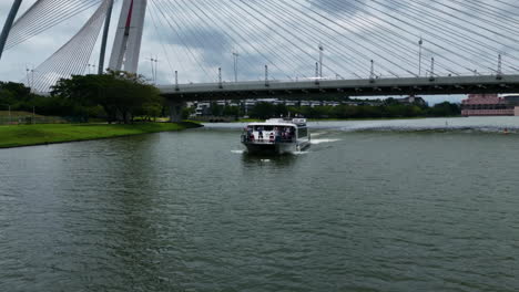 Drone-flying-in-front-of-a-tourist-ferry-driving-on-the-Putrajaya-Lake,-in-Malaysia