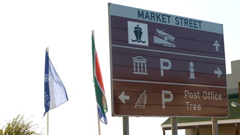 Tourism-road-sign-with-flags-flapping-next-to-it,-Mossel-Bay