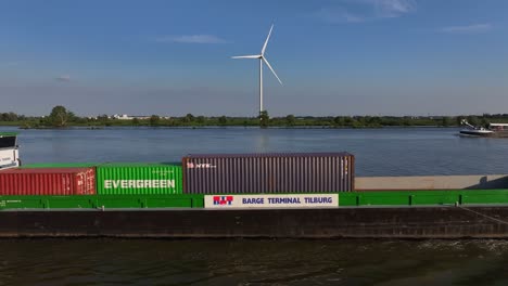 Dutch-container-ship-Tornado-moves-on-river-by-wind-turbine,-aerial