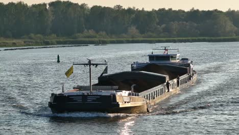 Dutch-freighter-ship-Kedia-transports-coal-on-river-at-golden-hour,-aerial-pan