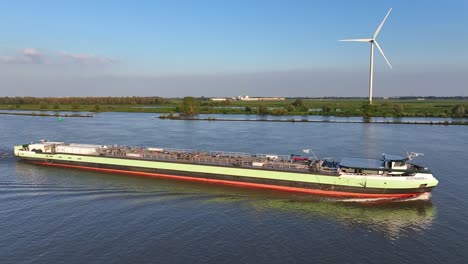 Tanker-ship-on-river-by-wind-turbine-in-Netherlands,-aerial-side-view