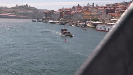 Slow-motion-footage-of-cruise-tour-boat-motoring-down-Duoro-River-on-bright-sunny-day-with-colourful-houses-buildings-along-Rivera,-Porto,-Portugal-2022