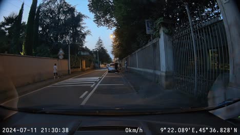 POV-a-parked-car-pulls-out-and-drives-down-narrow-streets-at-dusk,-dash-cam-video