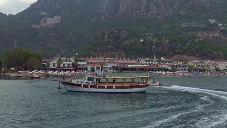 A-cloudy-but-warm-afternoon-in-Turunc,-Turkey-and-a-speed-boat-passes-a-tourist-passenger-boat-just-off-the-beach