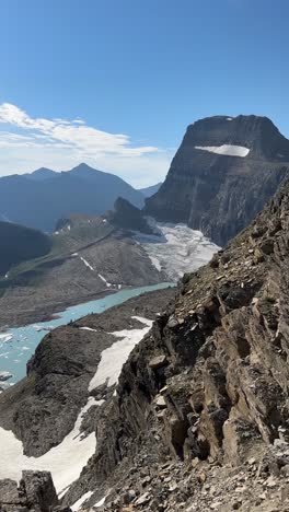 Vista-Vertical-De-Una-Mujer-Joven-De-Pie-Sobre-Un-Impresionante-Paisaje-Con-Glaciar-Y-Lago-Glacial-En-Un-Día-Soleado