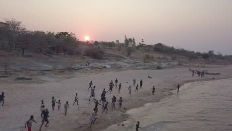 Local-children-playfully-react-to-drone-on-Lake-Malawi-beach,-sunset