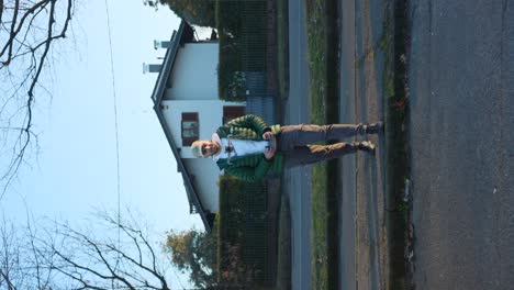 Video-Vertical-De-Un-Hombre-En-Una-Calle-Suburbana,-Con-Chaqueta-Verde-Y-Gorra,-Preparándose-Para-Lanzar-Un-Dron.