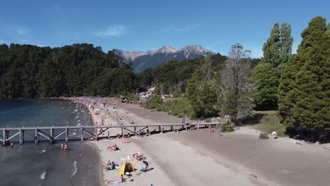 Luftaufnahme-In-Bodennähe-Mit-Menschen,-Die-Einen-Sonnigen-Tag-Am-Strand-Am-Ufer-Des-Nahuel-Huapi-Sees-In-Patagonien,-Argentinien-Genießen