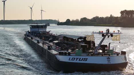 Dutch-tanker-ship-Lotus-on-river-with-wind-turbines-in-background,-aerial-pan