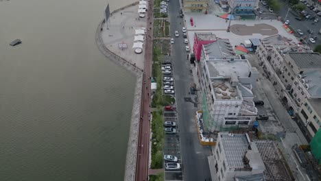 Aerial-footage-of-a-broad-walk-and-a-road-along-shops-located-at-Mingle-Lake-in-Daqing,-Heilongjiang-District-in-China