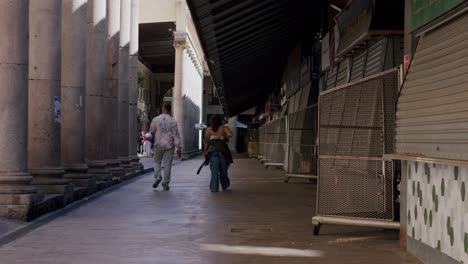 Couple-holding-hands-walking-through-a-quiet-alley-in-Barcelona,-sunlight-casting-shadows