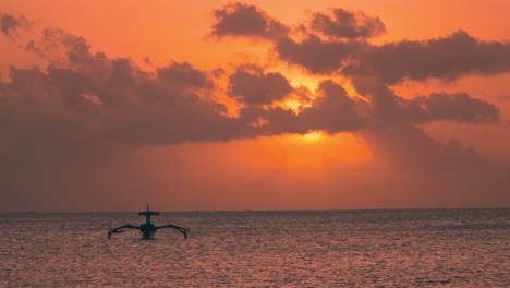 One-Outrigger-Boat-Balinese-Fishing-Vessel-Anchored-In-Sea-During-Dramatic-Sundown-in-Bali,-Indonesia